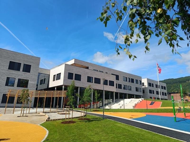 Fjelltun skole med skolegård, lekeplass og flagg en solrik dag